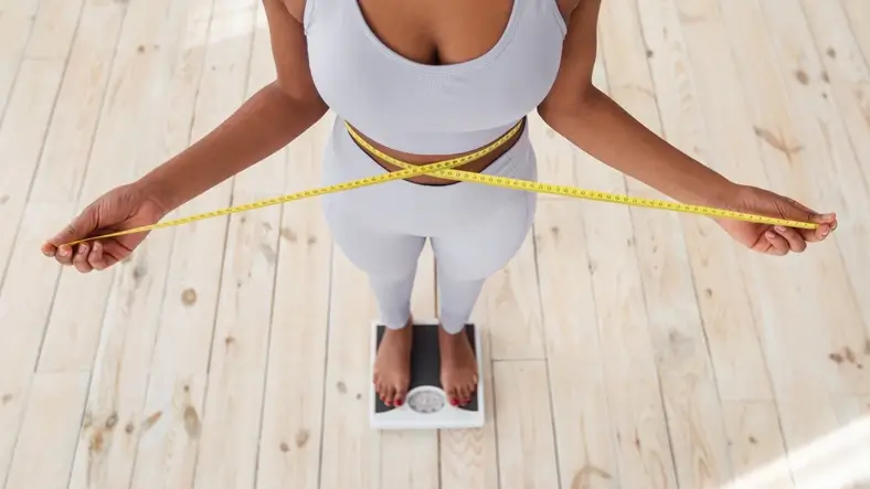 Woman standing on a scale and measuring her waist, representing medical weight loss and weight management